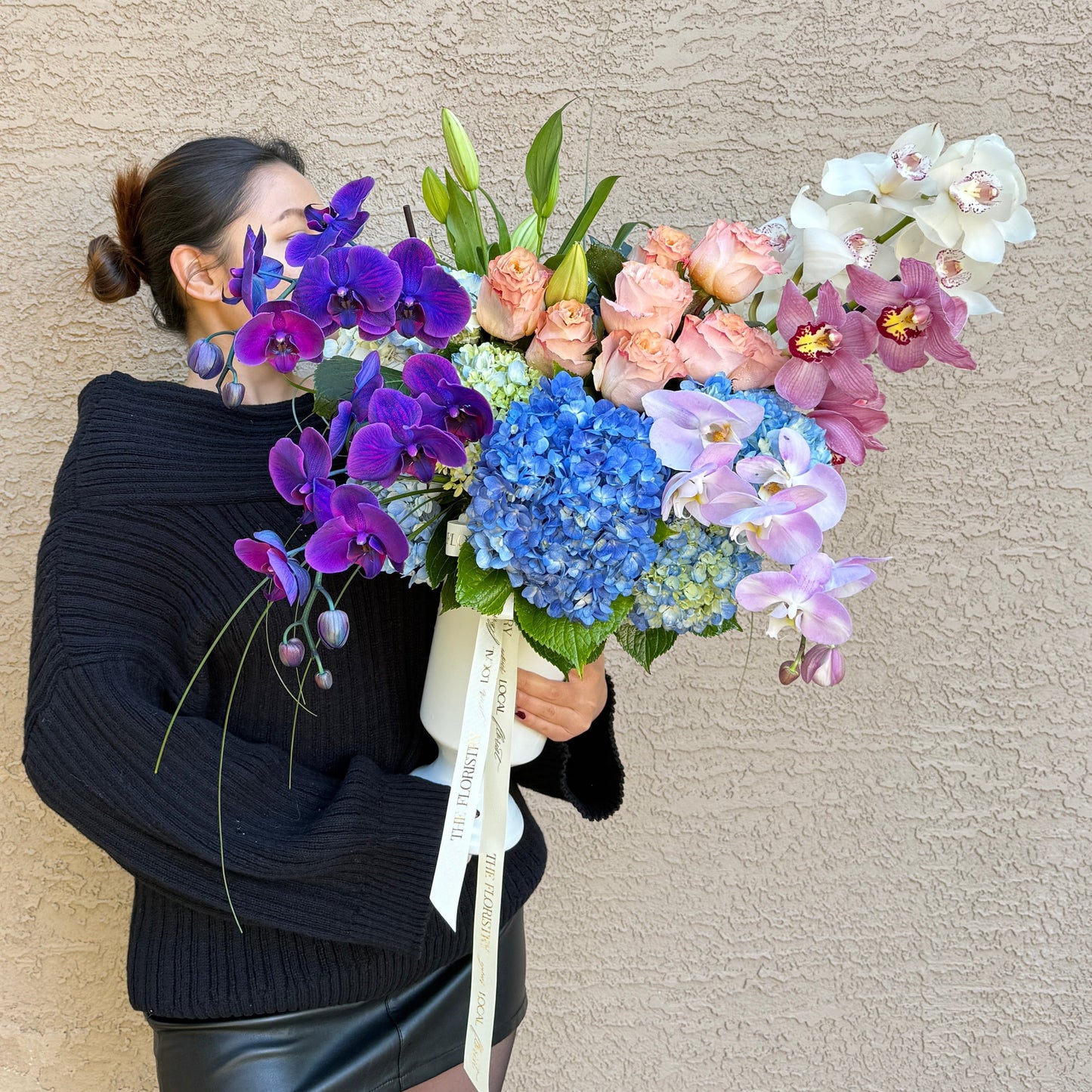 Person holding a luxury bouquet of flowers against a plain background