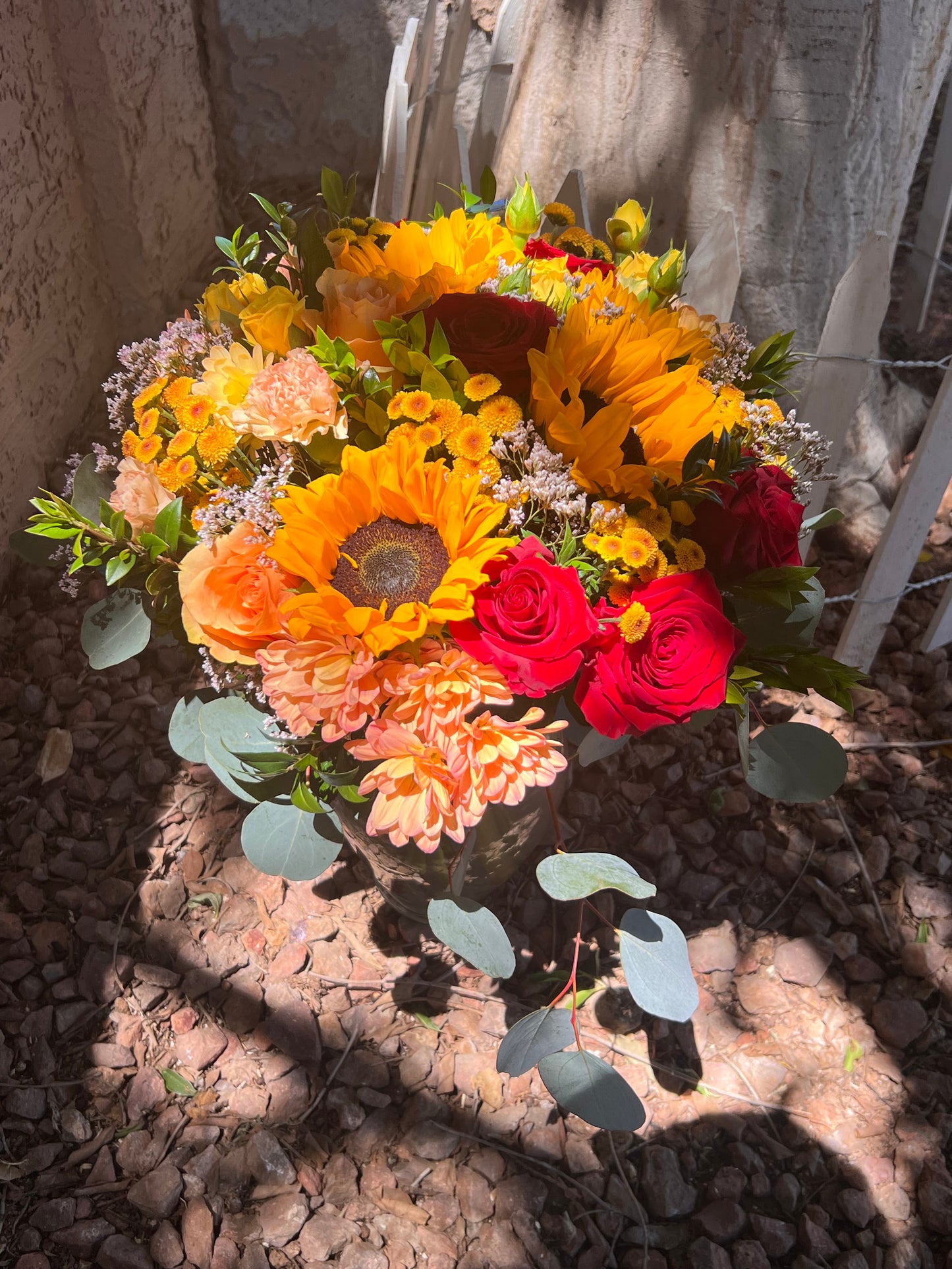 A vibrant Harvest Bouquet with a variety of flowers including roses and sunflowers, arranged in a clear glass vase, yellow, red, orange and warm tone.