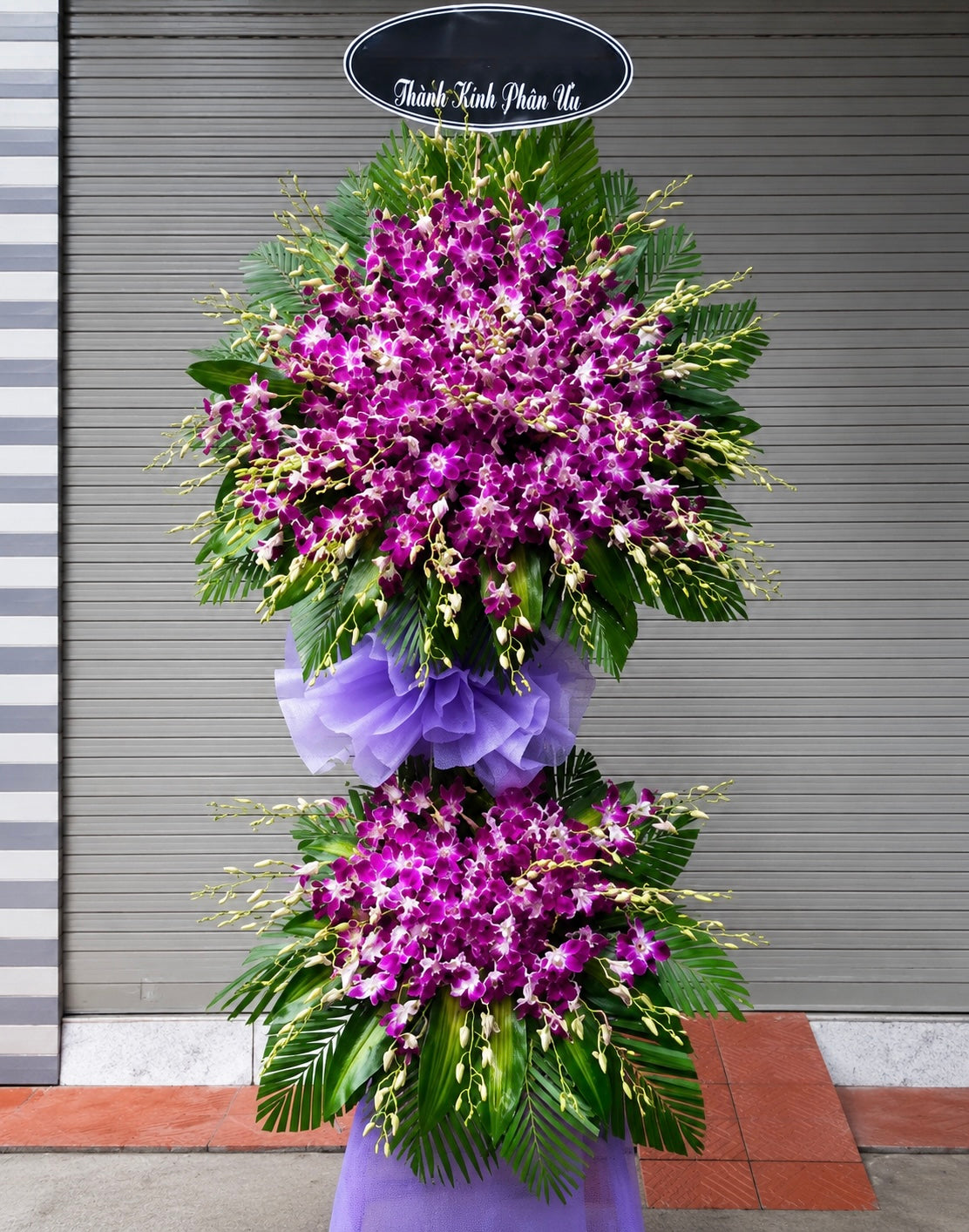 
Elegant purple orchid funeral floral stand with double-layer sympathy arrangement and tropical greenery accents.