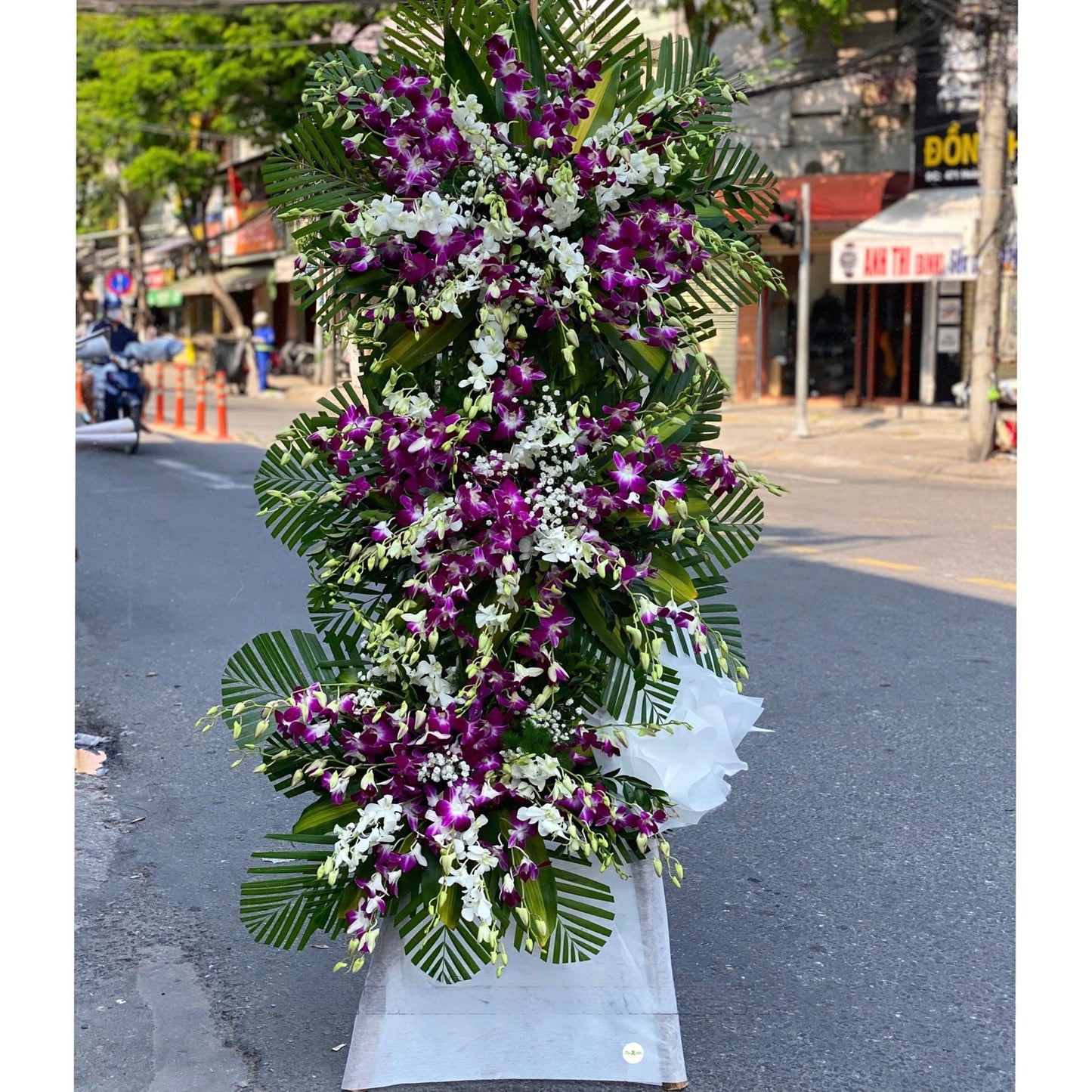Luxurious standing funeral tribute featuring vibrant purple orchids, palm leaves, and lavender wrapping.