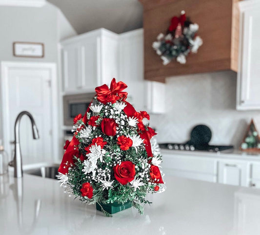 A Christmas tree arrangement with red roses and white baby's breath, placed on a counter in a home setting.