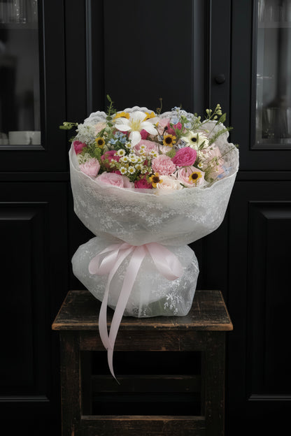 French garden-inspired bouquet with soft pink and lavender spring blooms wrapped in lace and tied with a satin ribbon