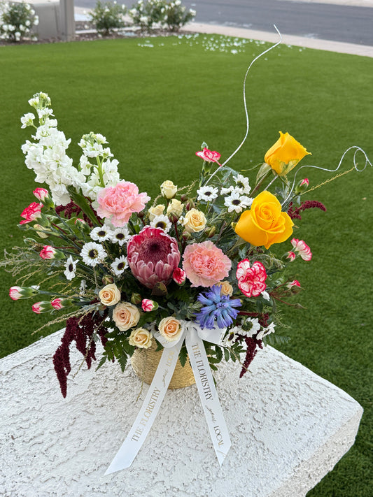 Spring mix floral centerpiece featuring fresh seasonal blooms in soft pastel and vibrant spring colors arranged in a low profile design.