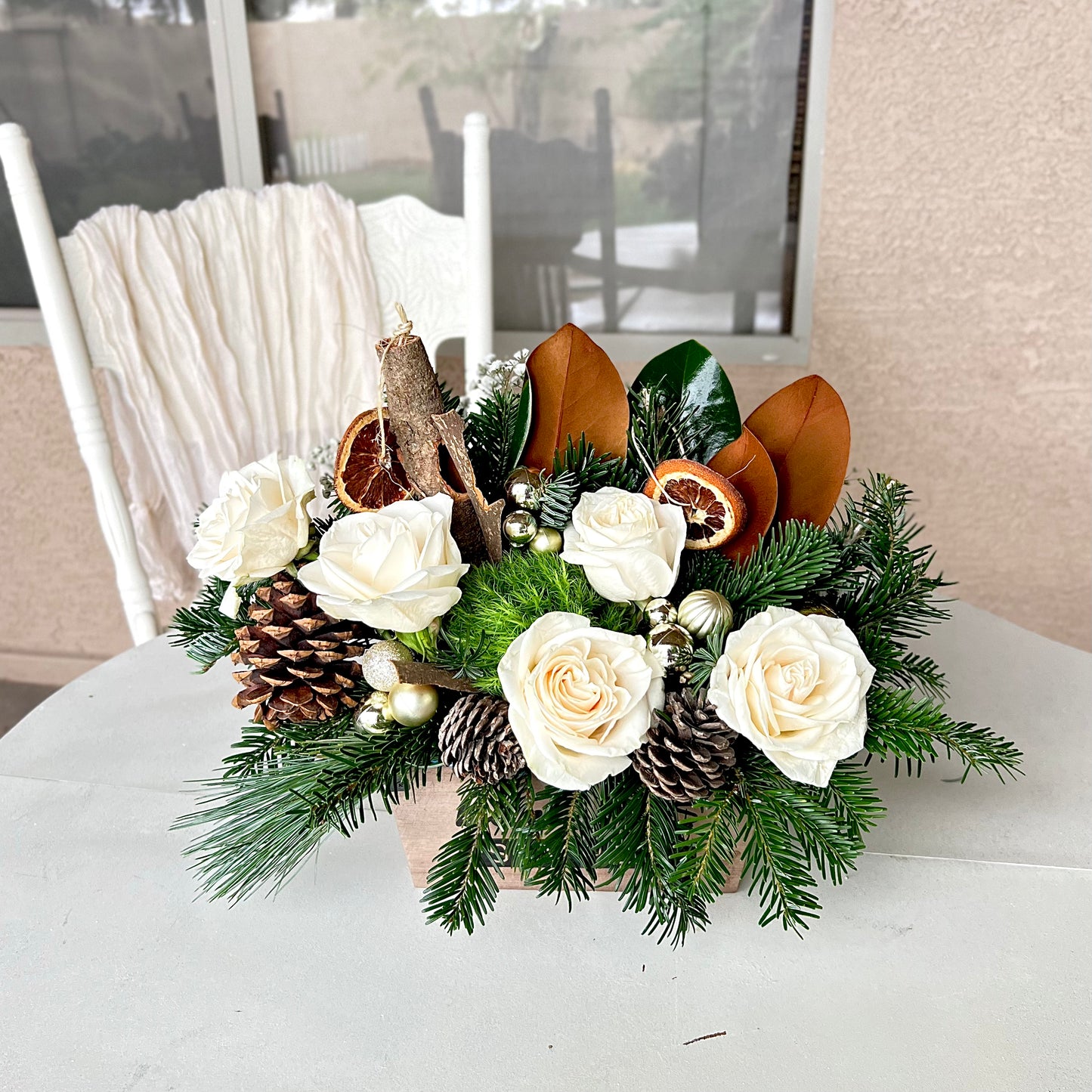 Festive Christmas centerpiece with white roses, silvery eucalyptus, pinecones, frosted pine branches, and delicate filler flowers.
