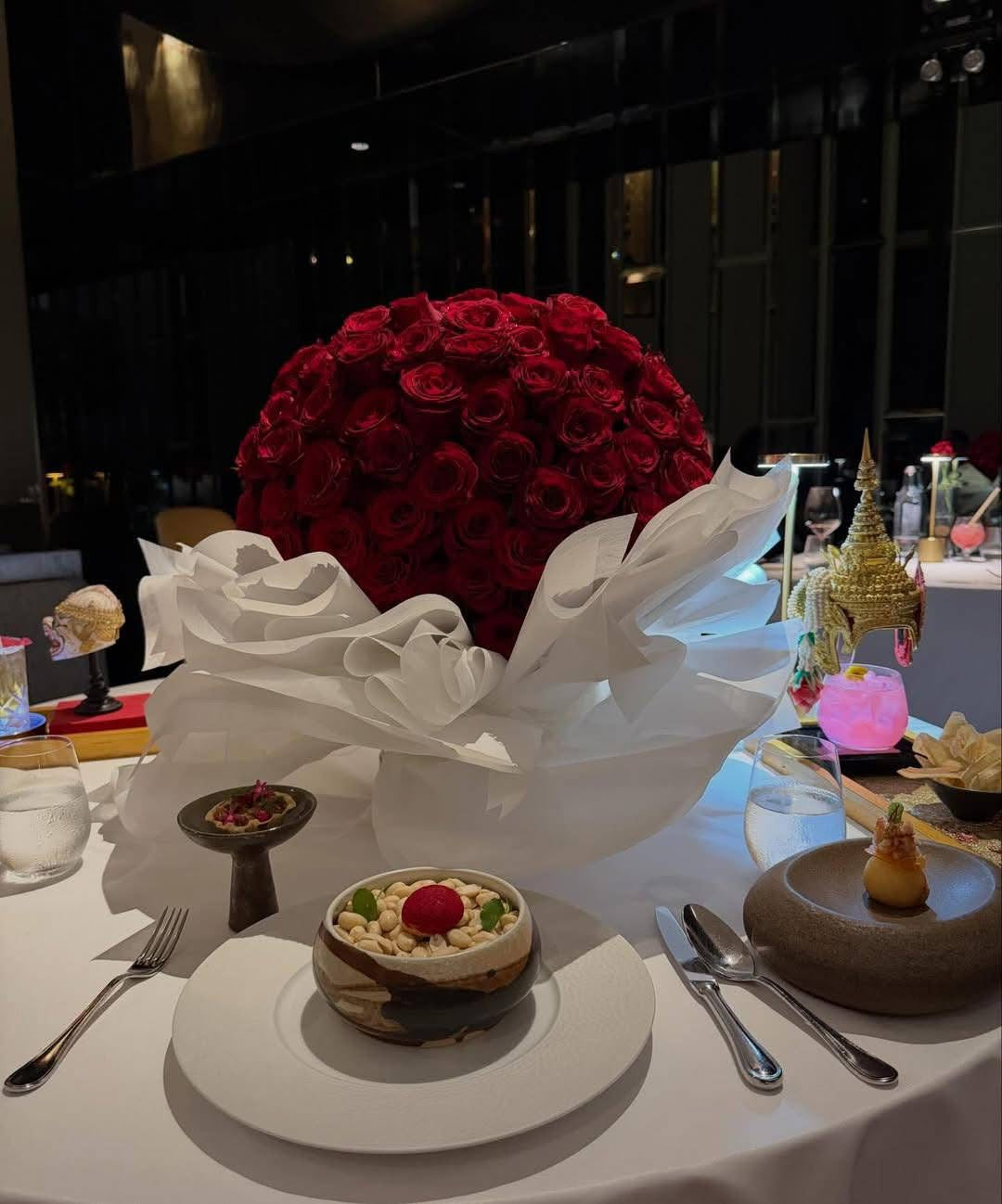 Luxury dome arrangement of premium red roses  wrapped in elegant white couture-style paper, displayed on a fine dining table, a romantic anniversary floral statement piece.
