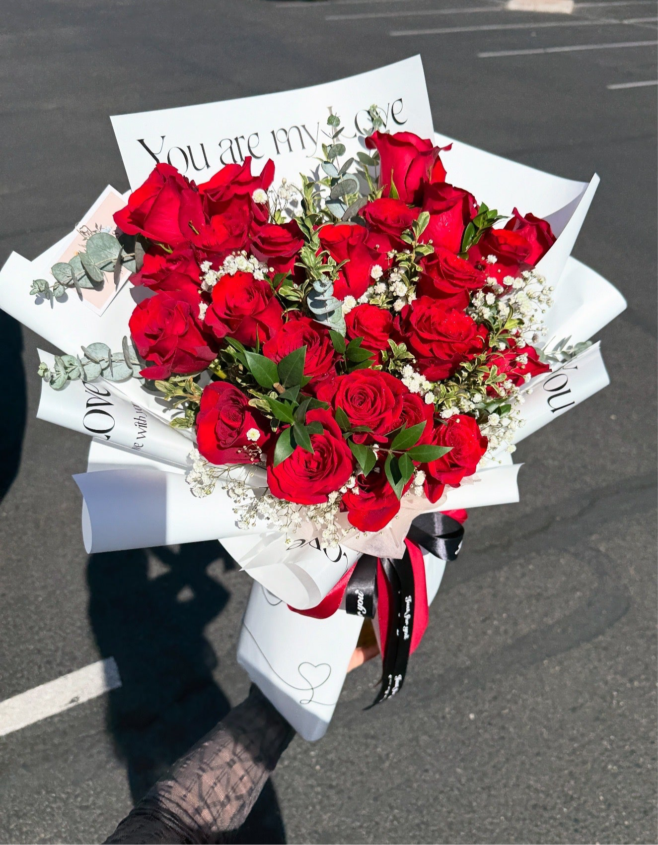 A bouquet of premium long stem red roses with white wrapping paper and decorative ribbons.