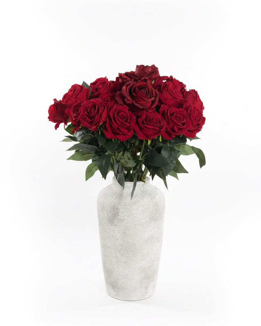 A bouquet of red roses with green leaves arranged in a textured, light gray ceramic vase, set against a plain white background.