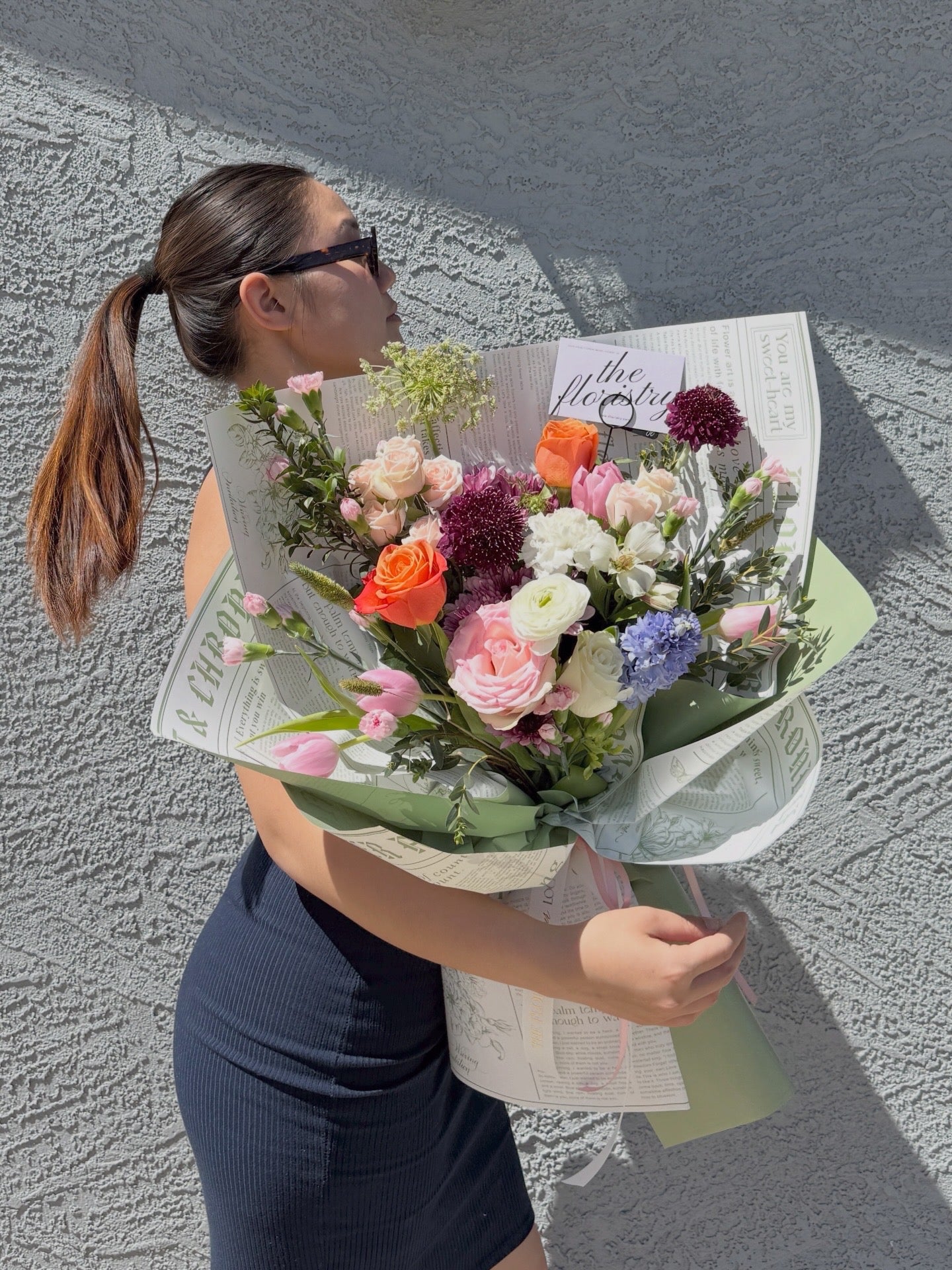 a large, vibrant bouquet of multicolored flowers wrapped in newspaper-style wrapped paper 