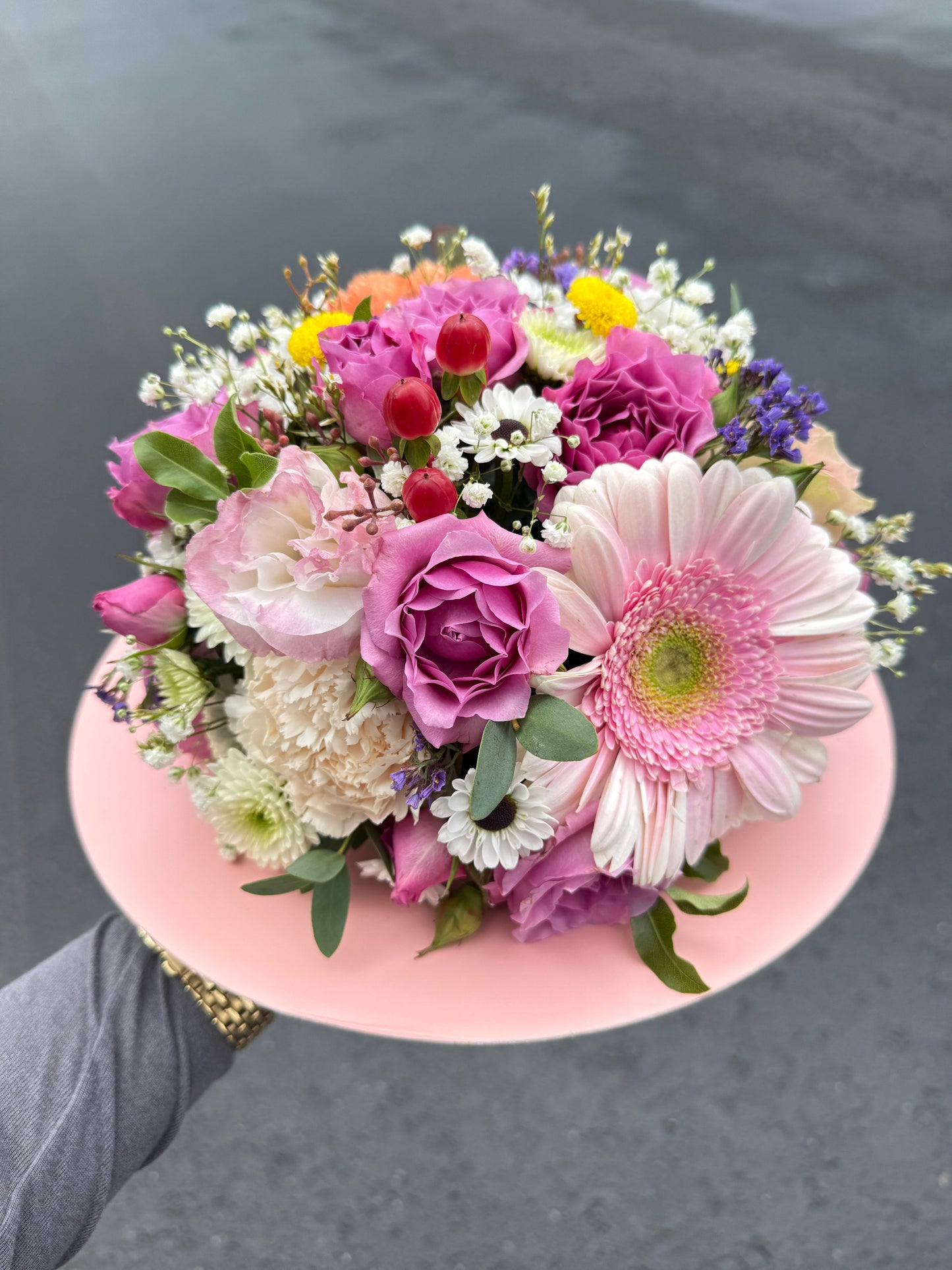 Bouquet of colorful flowers held by a person against a gray background