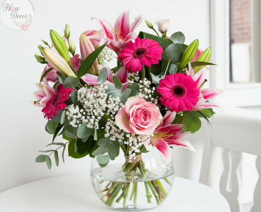 A glass vase containing a colorful bouquet of flowers including pink roses and other greenery