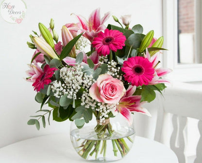 A glass vase containing a colorful bouquet of flowers including pink roses and other greenery