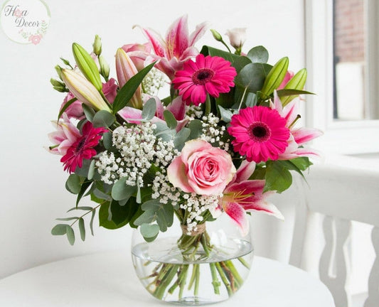 A glass vase containing a colorful bouquet of flowers including pink roses and other greenery