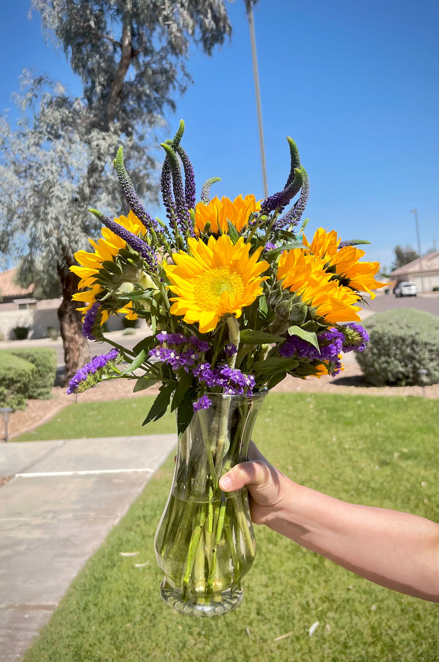 A vase with a bouquet of sunflowers and purple flowers.