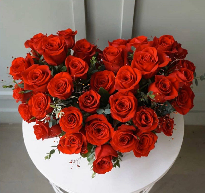 An arrangement of vibrant red roses arranged in a heart shape, presented on a white surface.