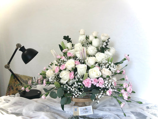 A floral arrangement featuring roses in a box, with a variety of other flowers and greenery, arranged on a table.