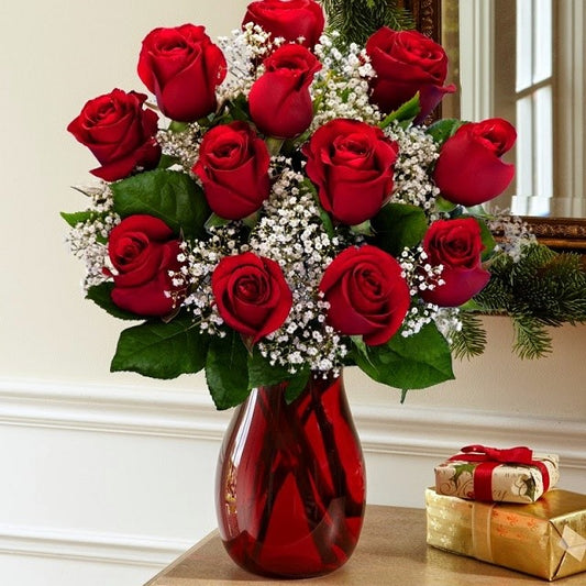 A bouquet of premium long stems red roses arranged in a clear red vase, with green leaves and white filler flowers for same day flower delivery