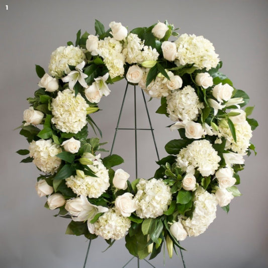 A wreath of white lilies and orchids with green leaves arranged on a circular frame.