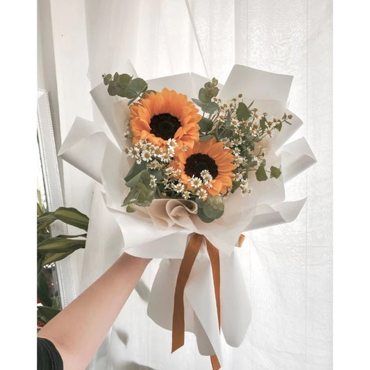 A bouquet of sunflowers wrapped in white paper with a brown ribbon.